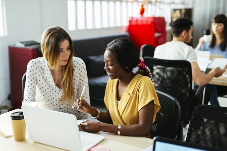 Two young professional women sitting in front of notes and a laptop at a hip local cafe